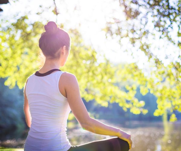Young woman in white top practicing yoga in beautiful nature. Meditation in morning sunny day. (photo; © Ganna Tugolukova | Dreamstime.com)